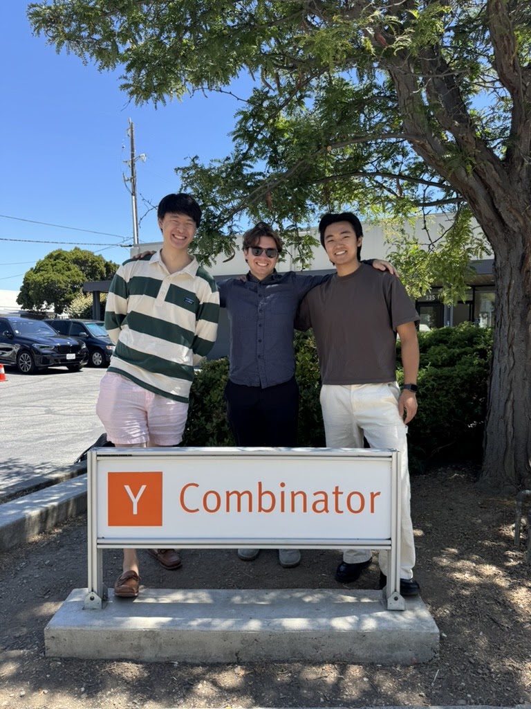 Three people standing behind the Y Combinator sign